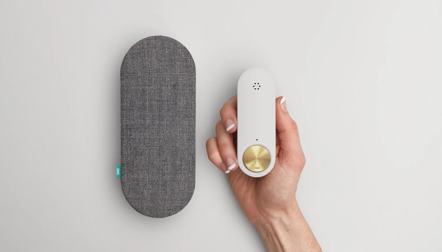 A hand holding the slim white Ome doorbell beside its grey fabric-covered chime speaker.